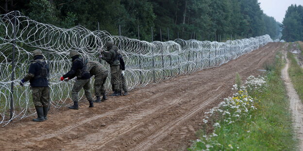 Polnische Sodlaten errichten einen hohen Zaun aus Maschendraht