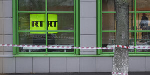 Das Logo des staatlichen russischen TV-Senders «Russia Today» ist am 27.10.2017 in Moskau (Russland) am Fenster des Firmenbüros zu sehen. Davor steht ein Baum, um den Absperrbanner gewickelt ist.