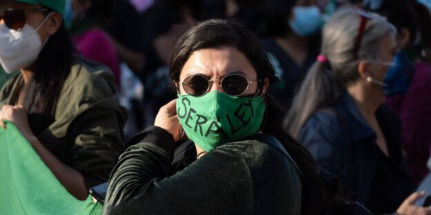 Eine Frau mit grüner Mundschutzmaske steht in einer menschenmenge