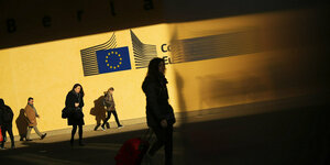 Passanten vor dem Logo des EU Parlaments
