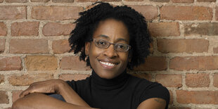 Jacqueline Woodson sitzt vor einer Backsteinmauer.