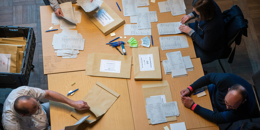 Wahlhelfer*innen sitzen an einem großen Tisch und werten Abstimmungszettel aus