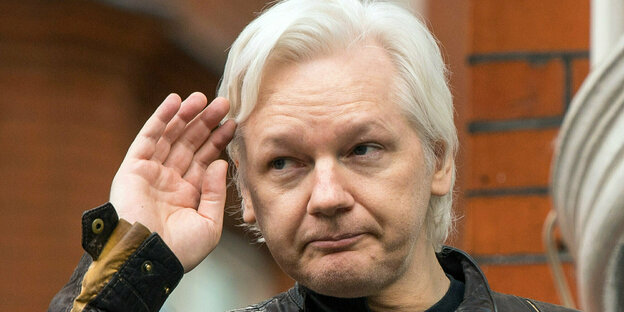 Julian Assange hebt eine Hand zu seiner Stirn