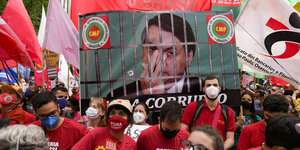 Rot gekleidete Menschen mit Fahnen vor einem Plakat mit Bolsonaro hinter Gittern.