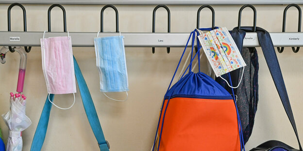 Masken und bunte Taschen hängen an einer Garderobe in einer Schule