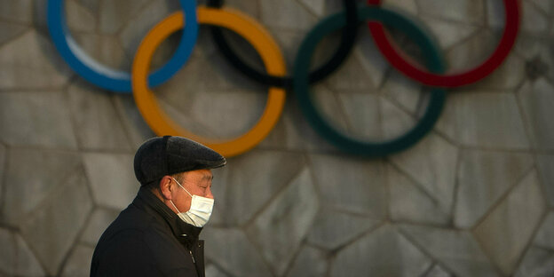Ein Einwohner von Peking passiert die Olympia-Ringe am Nationalstadio.