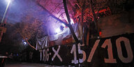 Ein schwarzes Transparent, darauf steht: Tag X 15/10. Im Hintergrund leuchtet Pyrotechnik