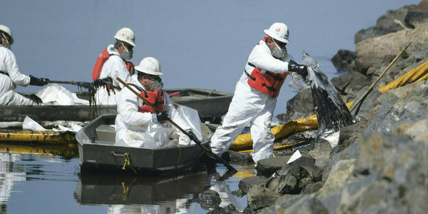 Männer in weissen Schutzanzüge in Booten entfernen Öl von Küstenfelsen