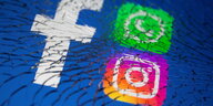 Symbole von Facebook, WhatsApp und Instagram auf einem Smartphone mit gesplittertem Bildschirm.