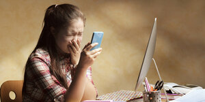 Weinendes Mädchen sizt am Schreibtisch und schaut auf sein Samrtphone