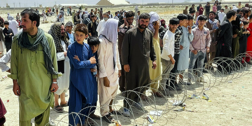 Männer stehen hinter einer Stacheldrahabsprerrung auf dem Flughafen Kabul