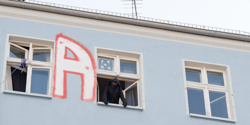 Vermummte Person guckt aus einem Fenster