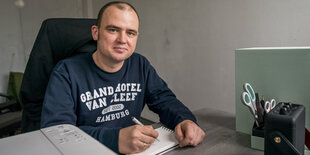 Ein Mann sitzt an einem Schreibtisch mit einem Block Papier und einem Stift in der Hand