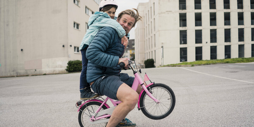 Vater und Tochter auf einem Kinderrad.