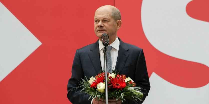 Olaf Scholz mit Blumenstrauß vor einem Mikrofon.