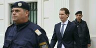 Österreichs Kanzler Sebastian Kurz im Anzug zwischen zwei Polizisten