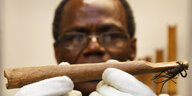 Wissenschaftler Ndzdno Awono hält mit weißen Handschuhen eine tütenförmige hölzerne Pfeife