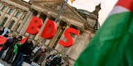 Rote Buchstaben "BDS" werden vor dem Bundestag in die Luft gehalten