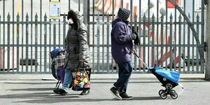 Zwei Frauen tragen Schutzmasken und ziehen ihre Trolleys mit Lebensmitteln