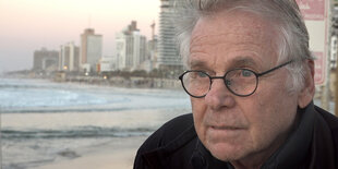 Porträt von Dany Cohn-Bendit. Im Hintergrund Strand und Skyline von Tel Aviv