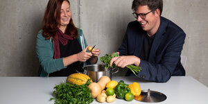 Eine Frau und ein Mann schneiden grün-gelbes Gemüse.