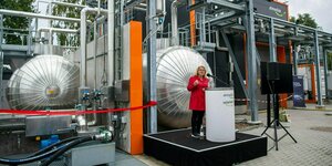Svenja Schulze steht vor einer Industrieanlage an einem Rednerpult
