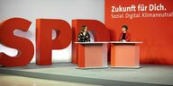 Jessica Rosenthal und Saskia Esken im Gespräch in einer Halle, die mit überlebensgroßen SPD Buchstaben geschmückt ist