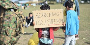 Ein junger Geflüchteter hält ein Pappschild mit der Aufschrift "SEARCHING FOR A SAFE HOME" hoch