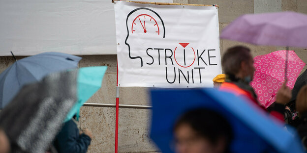 Streikende Pflegekräfte mit Regenschirm, auf einem Schild steht "Strike Unit"