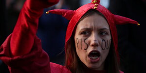 "PiS Out" hat sich eine junge Frau mit roter Kappe und Anzug auf das Gesicht gemalt