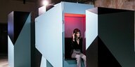 Eine Frau sitzt mit Kopfhörern in einer futuristischen Box und lauscht einer Künstlichen Intelligenz