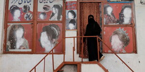 Eine verhüllte Frau steht vor einem Schönheitssalon, in dem auf Werbeplakaten, die Gesichter der Frauen übermalt wurden