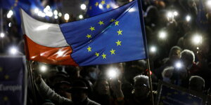 Eine Fahne ist zusammengenäht, ein Teil ist die ponische Flagge, ein Teil die Europafahne. Menschenmenge mit leuchtenden Handys