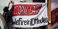 Ein Beschäftigter des Express-Lieferdiensts Gorillas klebt bei einer Demonstration vor der Firmenzentrale für bessere Arbeitsbedingungen ein Transparent mit der Aufschrift „Gorillas - We Fire in 10 Minutes“ an einer Wand fest.