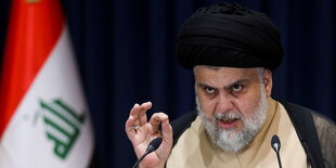 Der iranische Wahlsieger Muktada al-Sadr mit Turban und weißem Vollbart vor iranischer Flagge