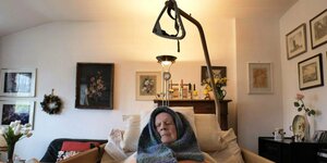 Alter Mann liegt in einem Pflegebett im Wohnzimmer mit einem Schal um den Kopf