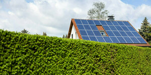 Ein einfamilienhaus mit Solarzellen auf dem Hausdach steht hinter einer grünen Hecke