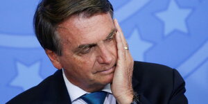 Bolsonaro mit gesenktem Blick, den Kopf auf die Hand gestützt.