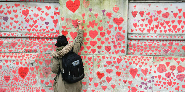 Eine Frau zeichnet ein Herz an die National Covid memorial Wall