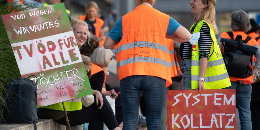 Teilnehmer an einer Demonstration von Beschäftigen der landeseigenen Berliner Krankenhäuser Vivantes und Charité stehen vor dem Hochhaus der Charitè. Auf einem Schild steht "Systemkollatz".