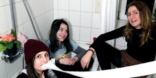 Die drei Musikerinnen der Band Riot Spears sitzen gequetscht im Badezimmer und haben Spaß mit Klopapier