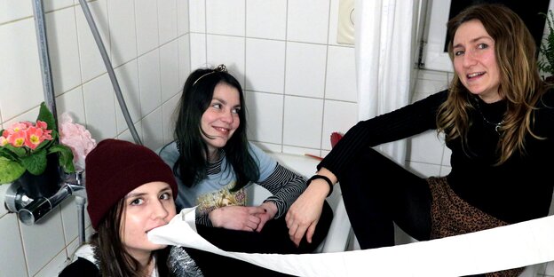 Die drei Musikerinnen der Band Riot Spears sitzen gequetscht im Badezimmer und haben Spaß mit Klopapier