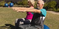 Zwei ältere Menschen sitzen auf einem Gynastikball und strecken die Arme im Rechten Winkel von sich
