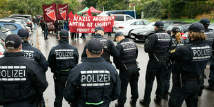 Eine Gruppe von Polizisten beobachtet eine Kundgebung: Auf dem mitgeführten Transparent steht: Nazis angreifen Andifa ist legitim