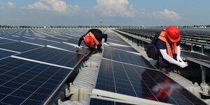 Ingenieure mit roten Helmen arbeiten an Solarpanelen auf einer Solarfarm