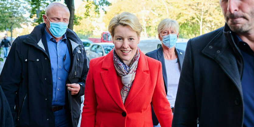 Franziska Giffey mit rotem Mntel umringt von Menschen mit Gesichtsmaske