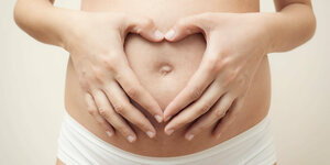 Zwei Hände auf einem schwangeren Bauch formen ein Herz