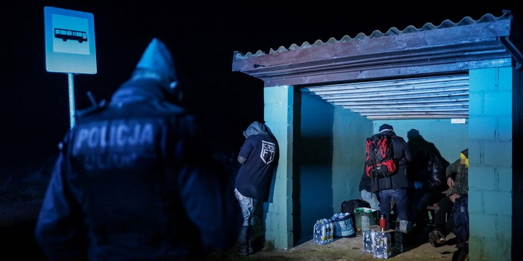 Menschen im Dunkeln in einer Bushaltestelle, davor Polizei.