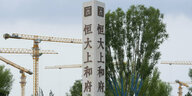 gelbe Baukränen und ein chinesischer Schriftzug auf einer Säule