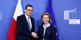 Ursula von derr Leyen und Mateusz Morawiecki schütteln sich vor einer blauen Wand mit polnischer Fahne die Hände